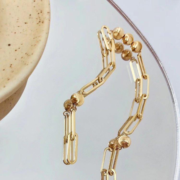 Gold chain bracelet with spherical beads on a neutral background