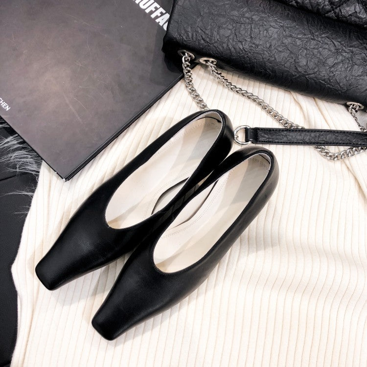 Black pointed-toe shoes on a textured surface with a black handbag and book in the background.