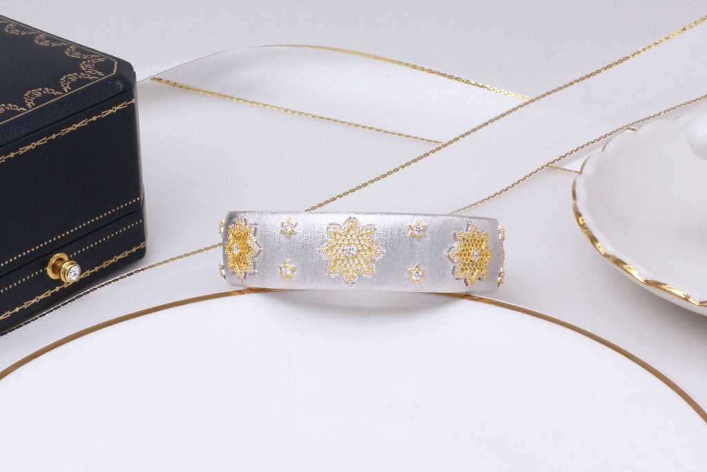 Decorative hair clip with gold patterns on a white surface with a black box and saucer.