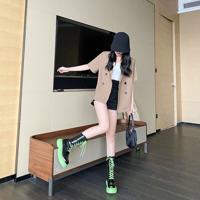 Woman in a beige coat and black hat standing on a wooden bench in a room with a television.