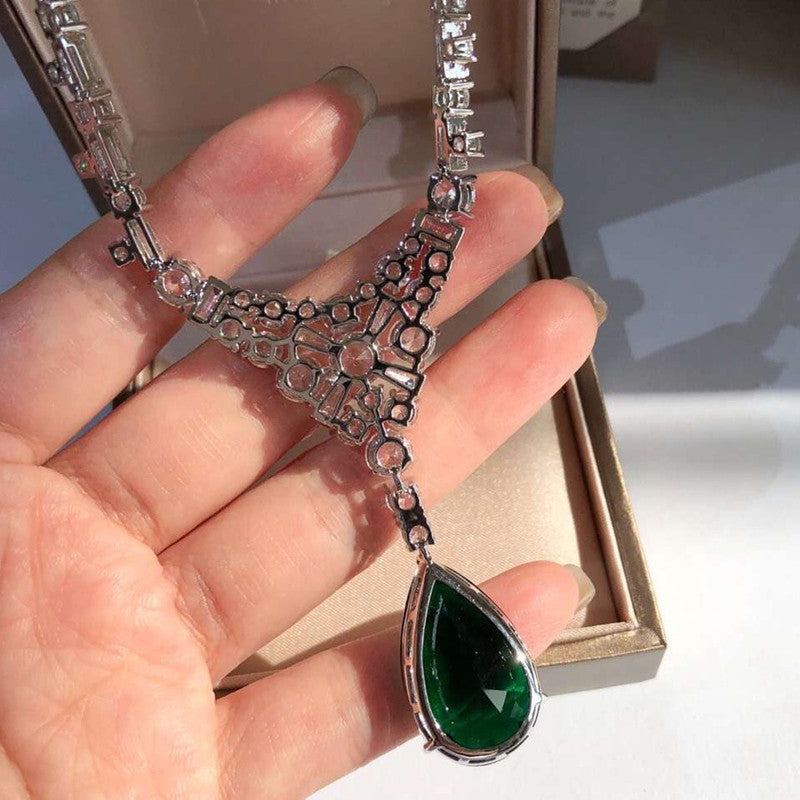 Silver necklace with a green pendant held by a hand