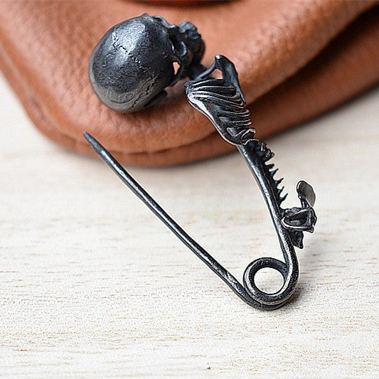 Decorative brooch with skull and fish design on a wooden surface