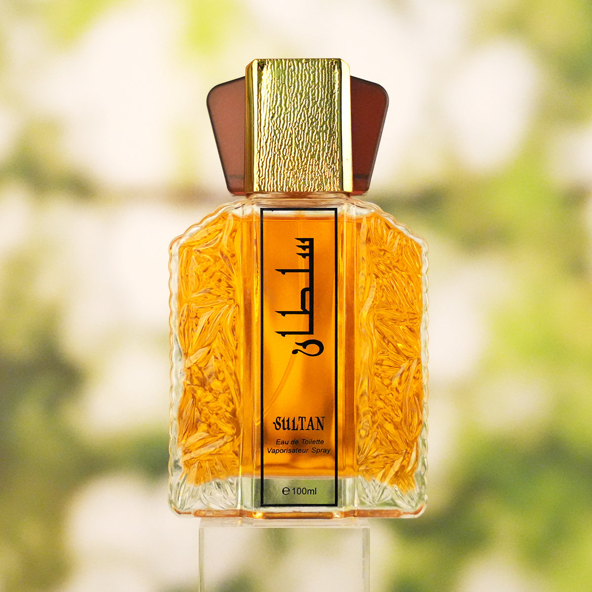 Perfume bottle with gold cap and intricate design on a blurred natural background