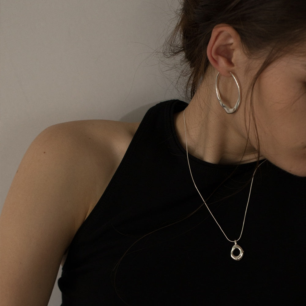 Person wearing a silver hoop earring and necklace against a neutral background