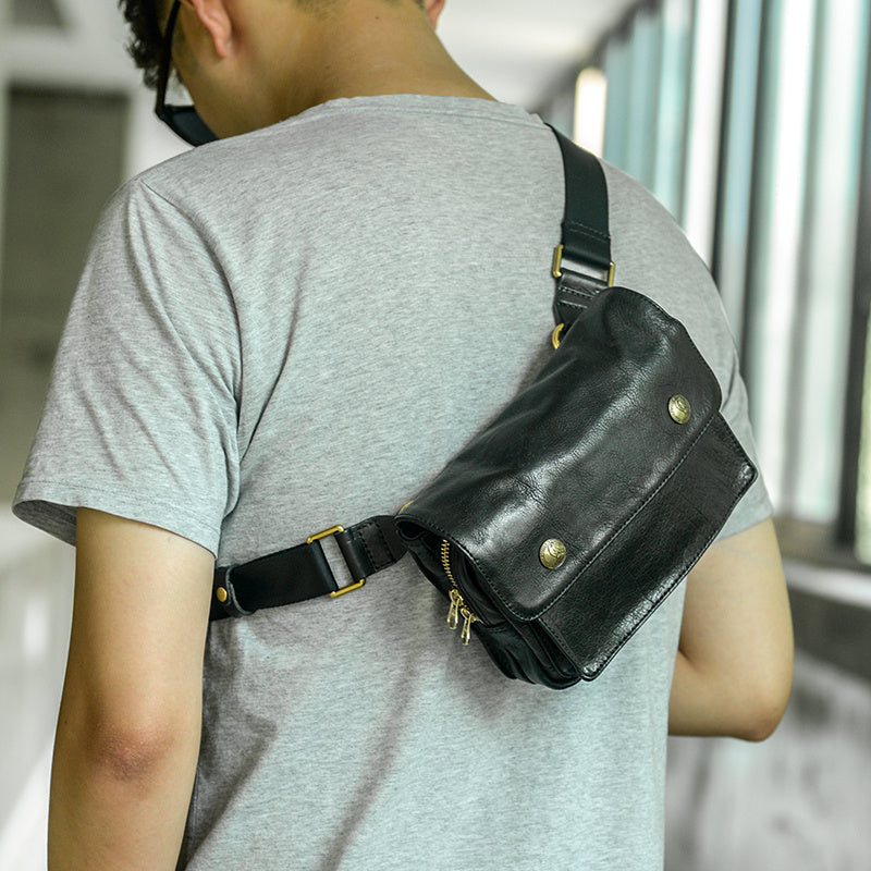 Person wearing a black leather crossbody bag with gold accents.