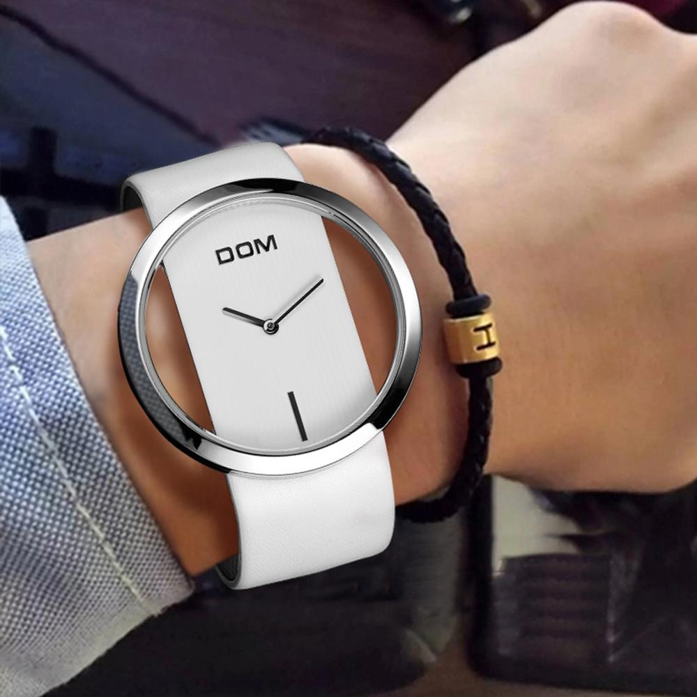 White wristwatch with silver case on a person's wrist, wearing a black and gold bracelet.