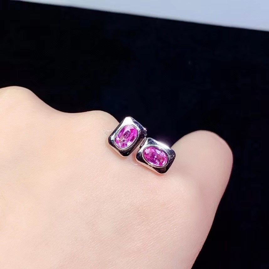 Pink gemstone stud earrings on a hand against a black background
