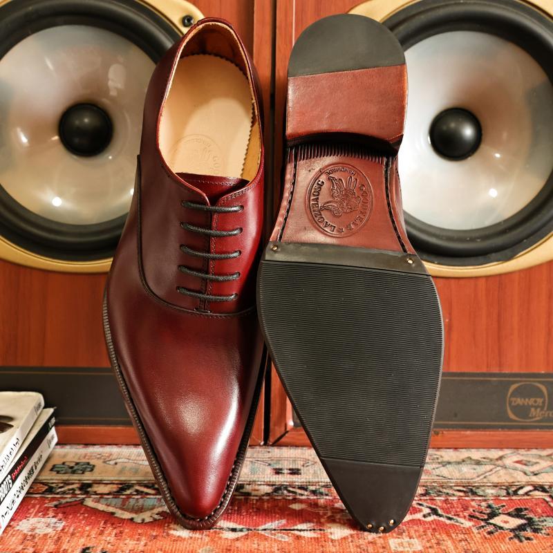 Brown leather dress shoes with a visible brand logo on a patterned rug.