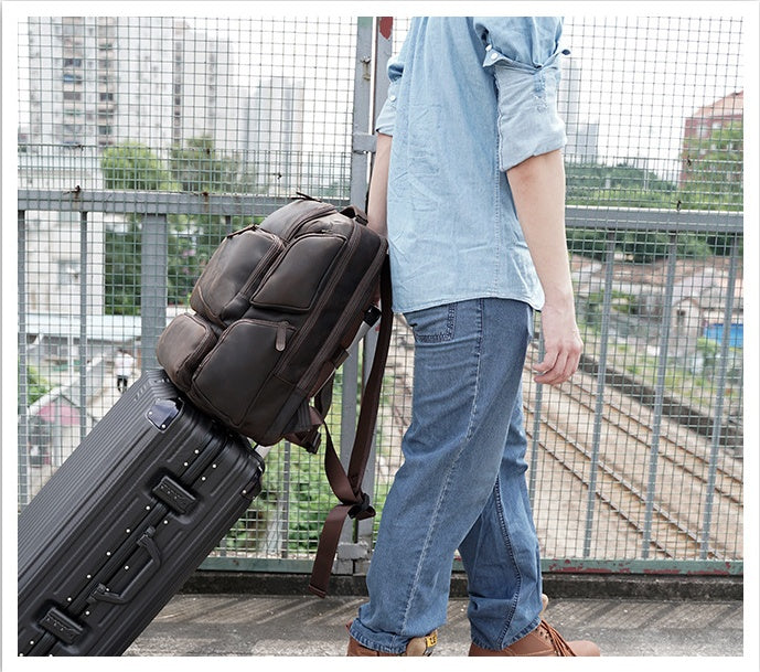 Person pulling a suitcase with a backpack over a metal fence.