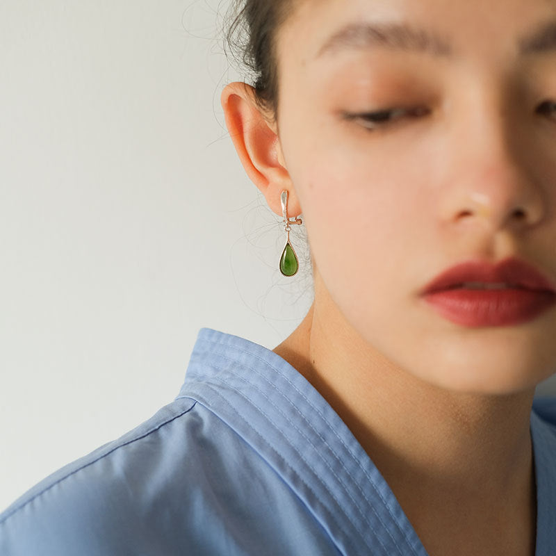 Close-up of a person wearing a green teardrop earring with a plain background