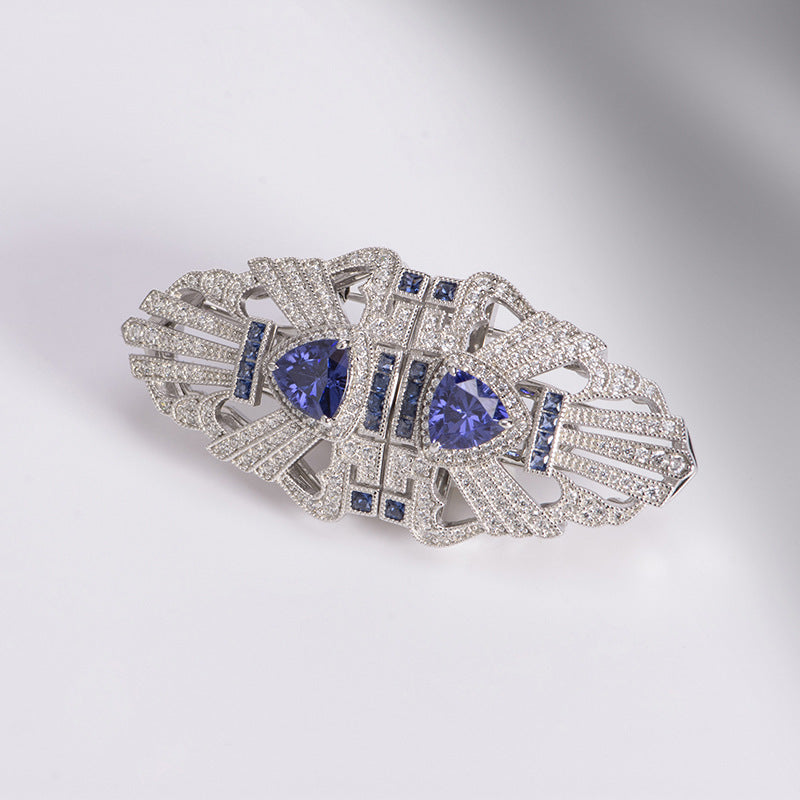 Elegant brooch with blue gemstones and diamond accents on a gradient background