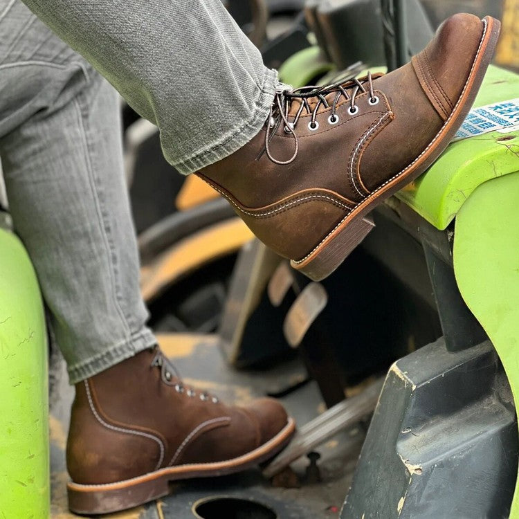 Brown leather boots worn by a person sitting on a green vehicle seat.