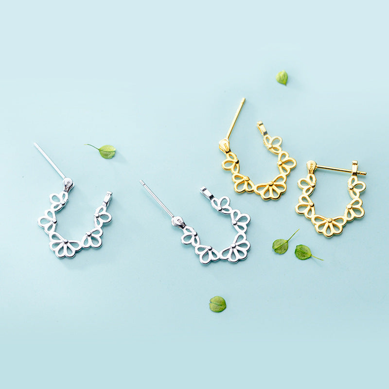 Gold and silver earrings on a light blue background with small green leaves.