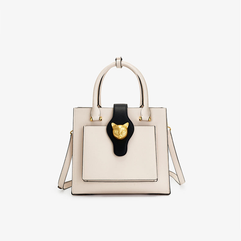 Beige handbag with black handle featuring a gold emblem on a white background