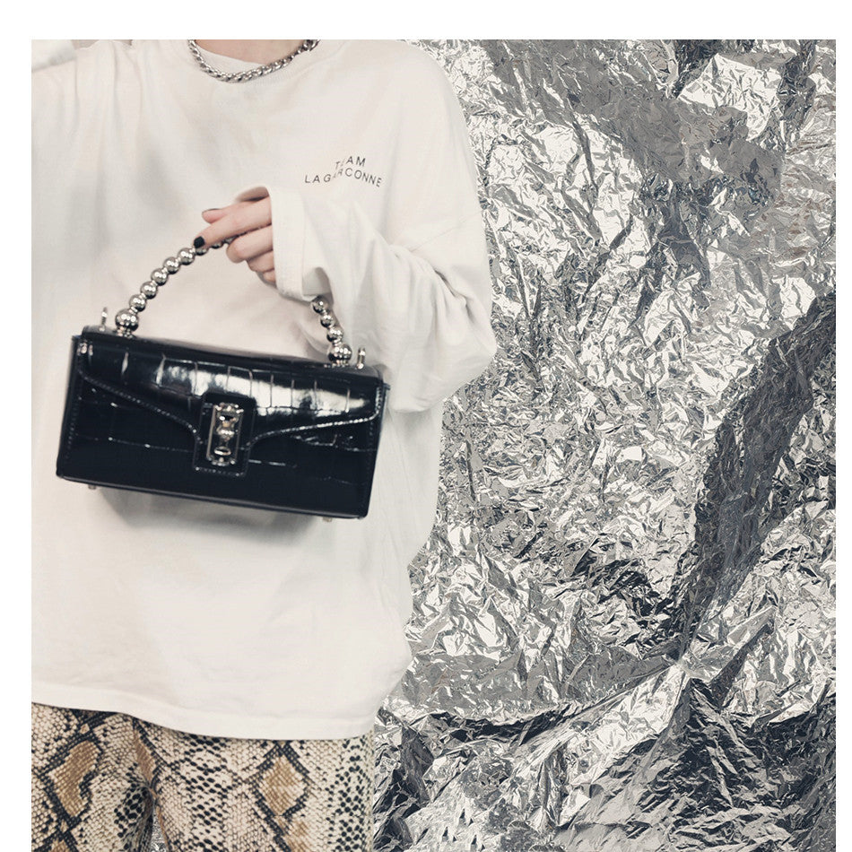 Person holding a black handbag against a silver foil background