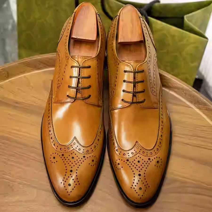 Pair of tan leather dress shoes with brogue pattern on a wooden surface.