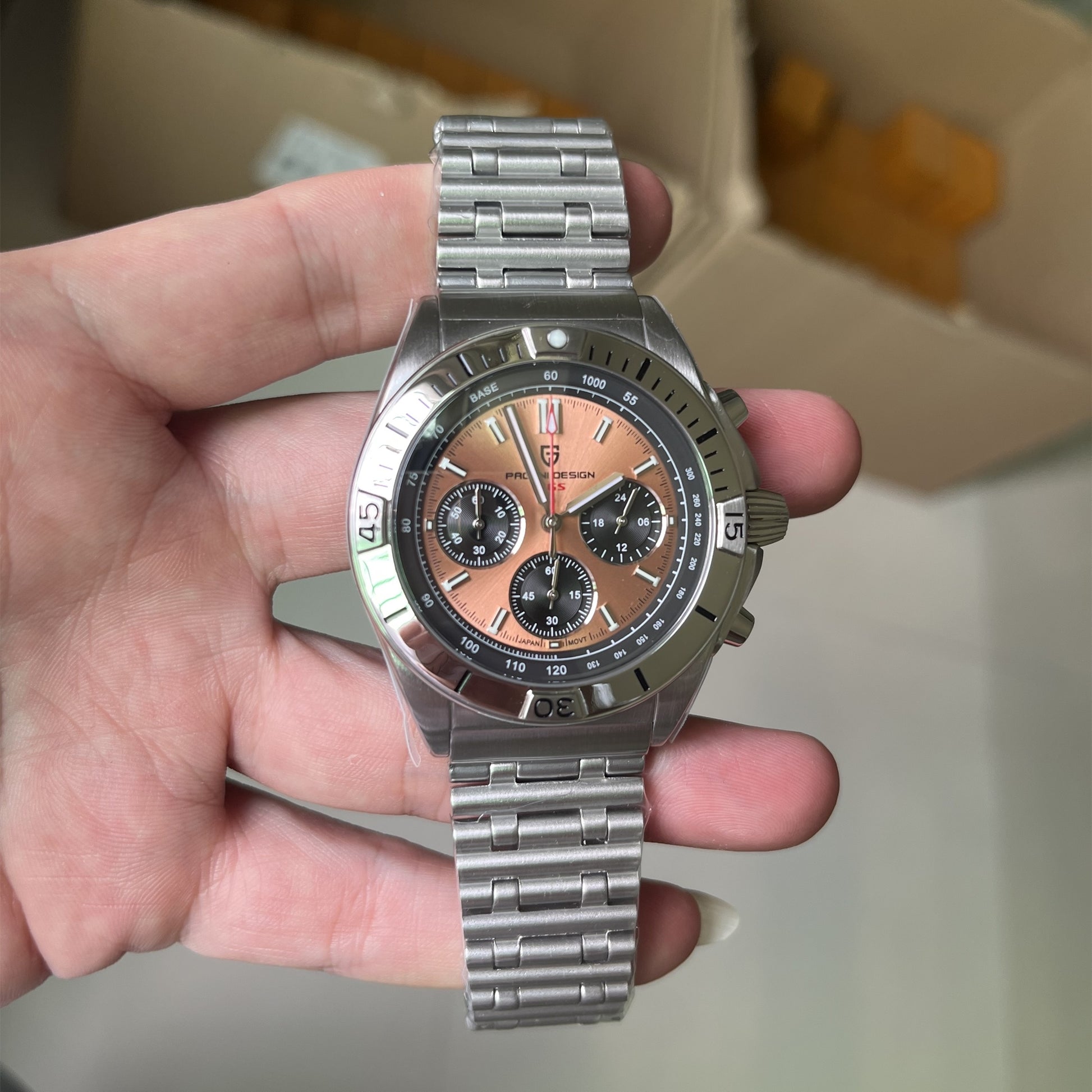 Hand holding a silver watch with a detailed face against a neutral background