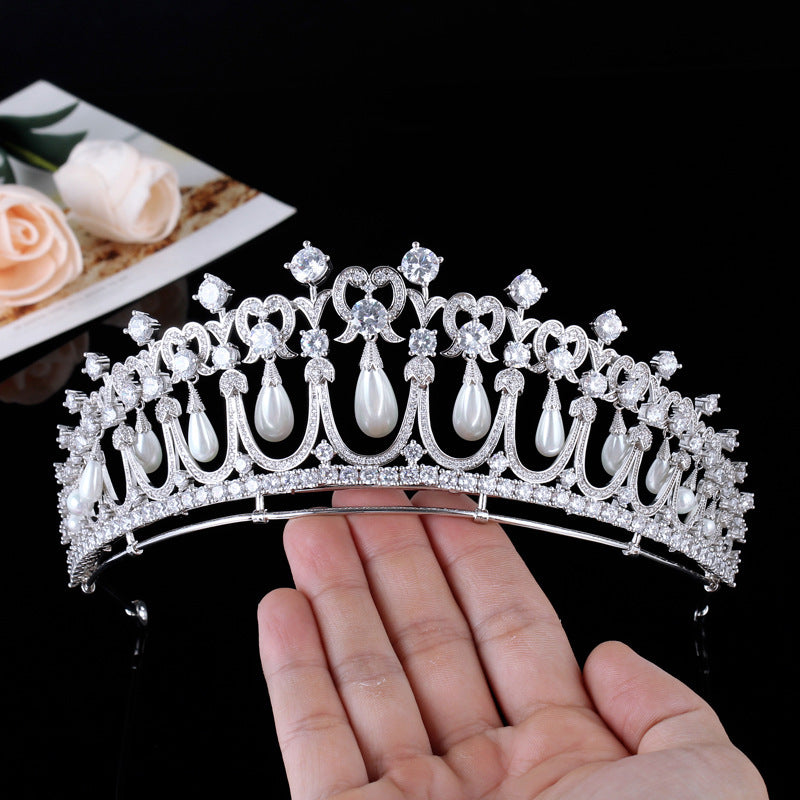 Silver tiara with pearls held in a hand against a black background