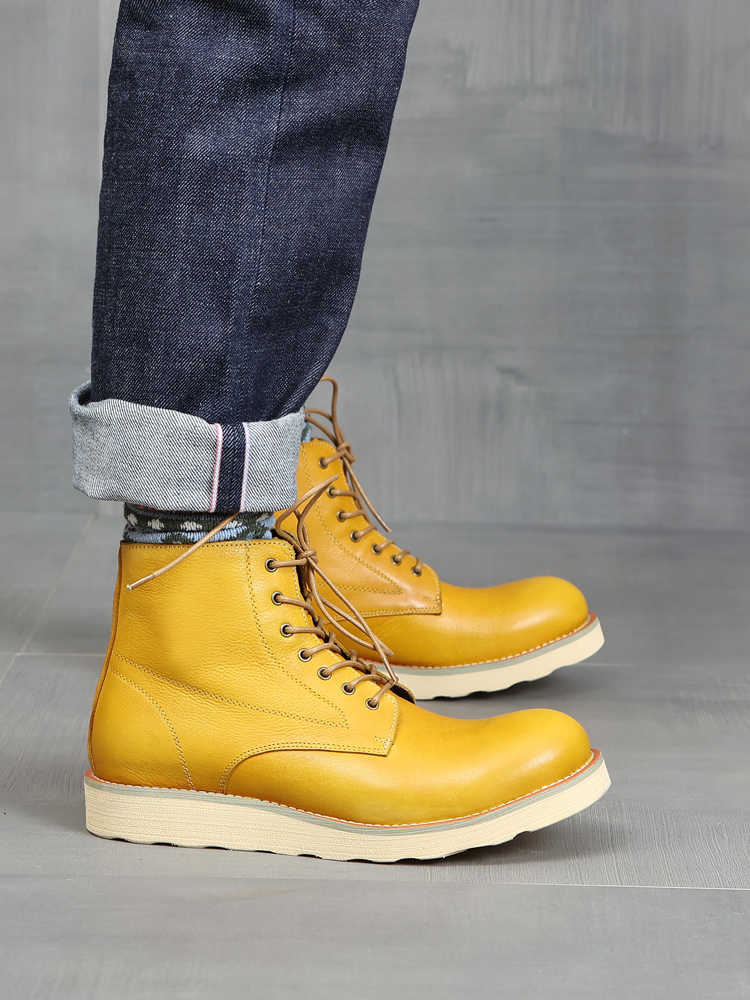 Yellow leather boots worn with blue jeans on a gray background