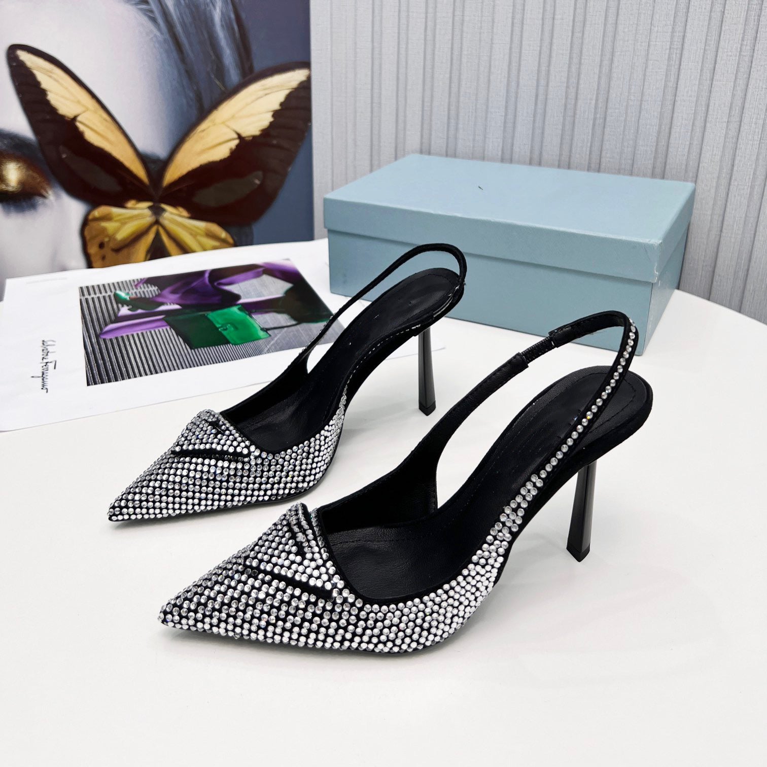 Black high-heeled shoes with silver embellishments on a white surface with a blue box and butterfly decoration.