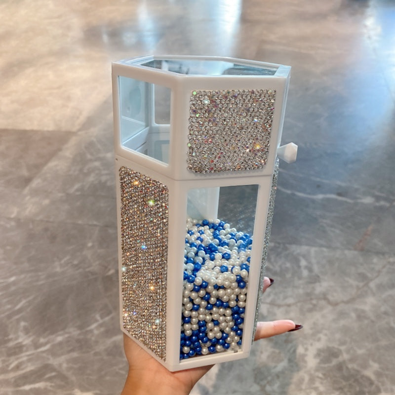 Decorative container with blue and white beads inside, held by a hand on a marble surface.