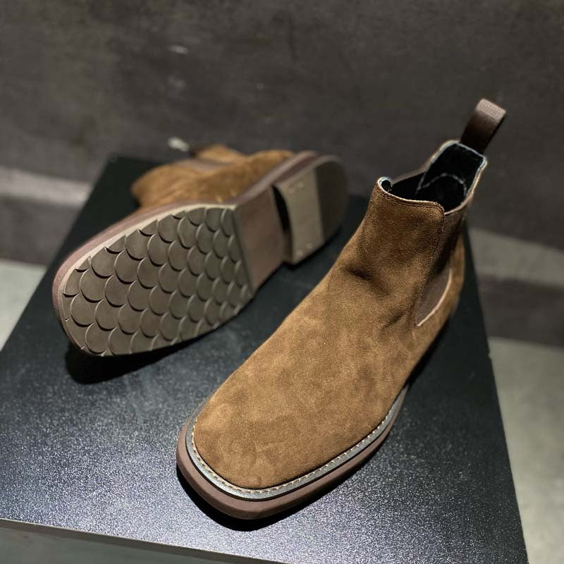 Brown suede Chelsea boots on a dark surface with a gray background