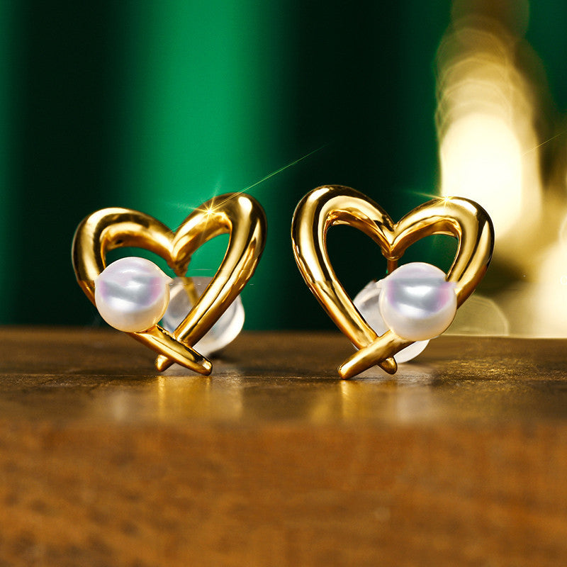 Gold heart-shaped earrings with pearls on a wooden surface.