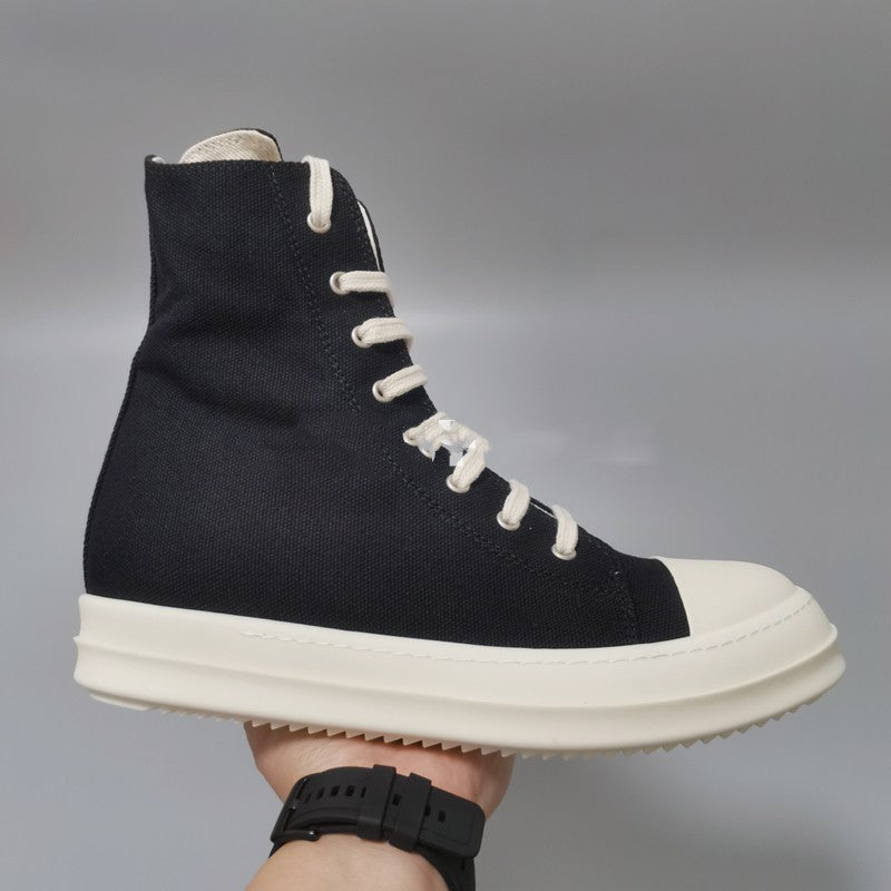Black high-top sneaker with white laces and sole held by a hand against a gray background