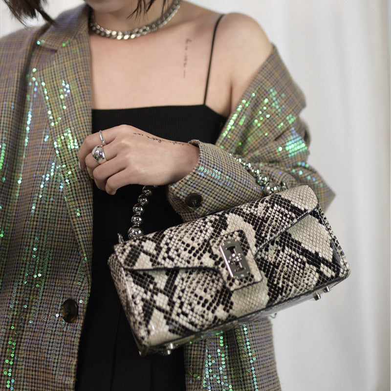 Person holding a snake print handbag with a sequin jacket