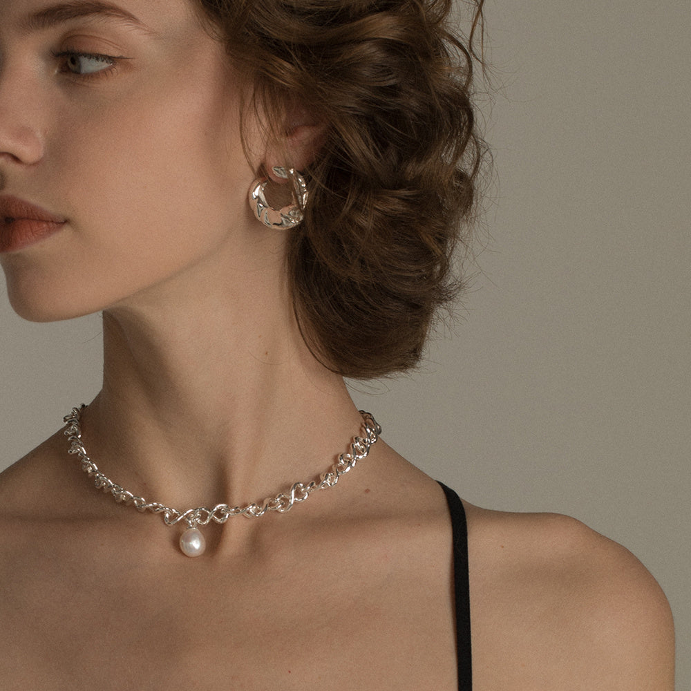 Close-up of a woman wearing a silver necklace with a pearl pendant and matching earrings.