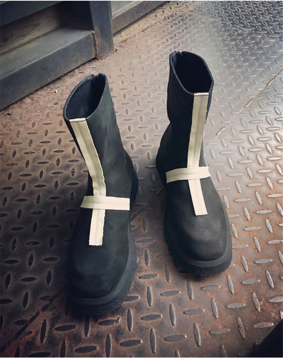 Pair of black rubber boots with white straps on a textured metal surface