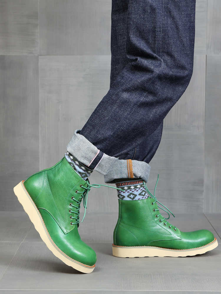 Green leather boots worn with dark jeans and patterned socks on a gray tiled floor.