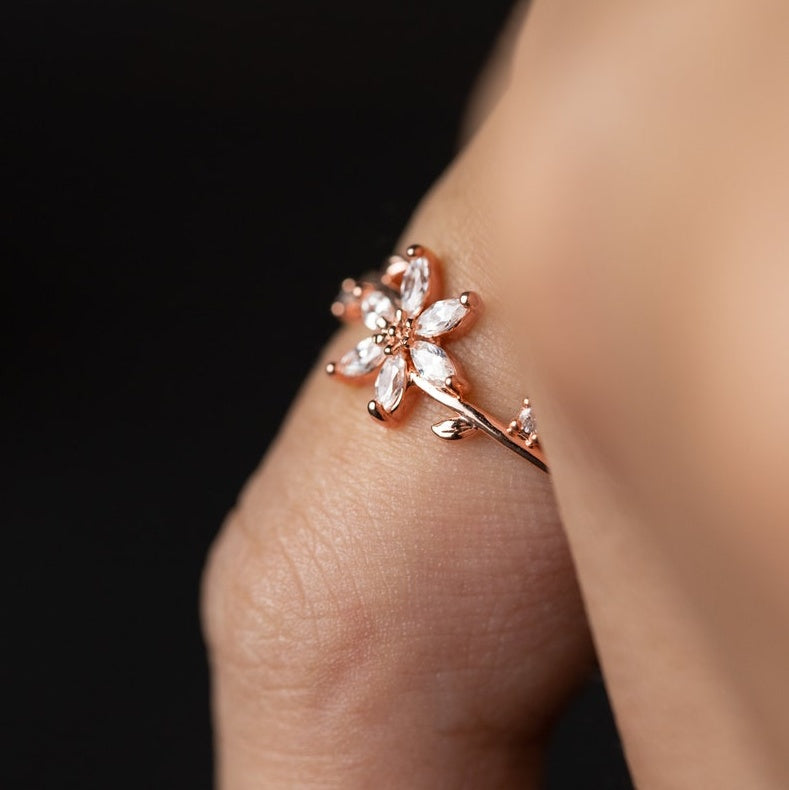 Rose gold floral earring on a person's ear against a black background