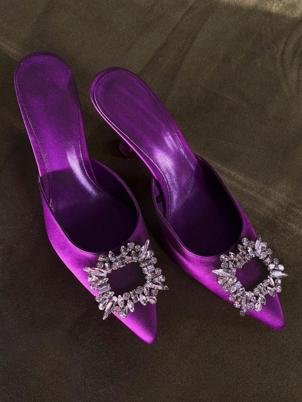 Purple high-heeled shoes with decorative embellishments on a brown surface