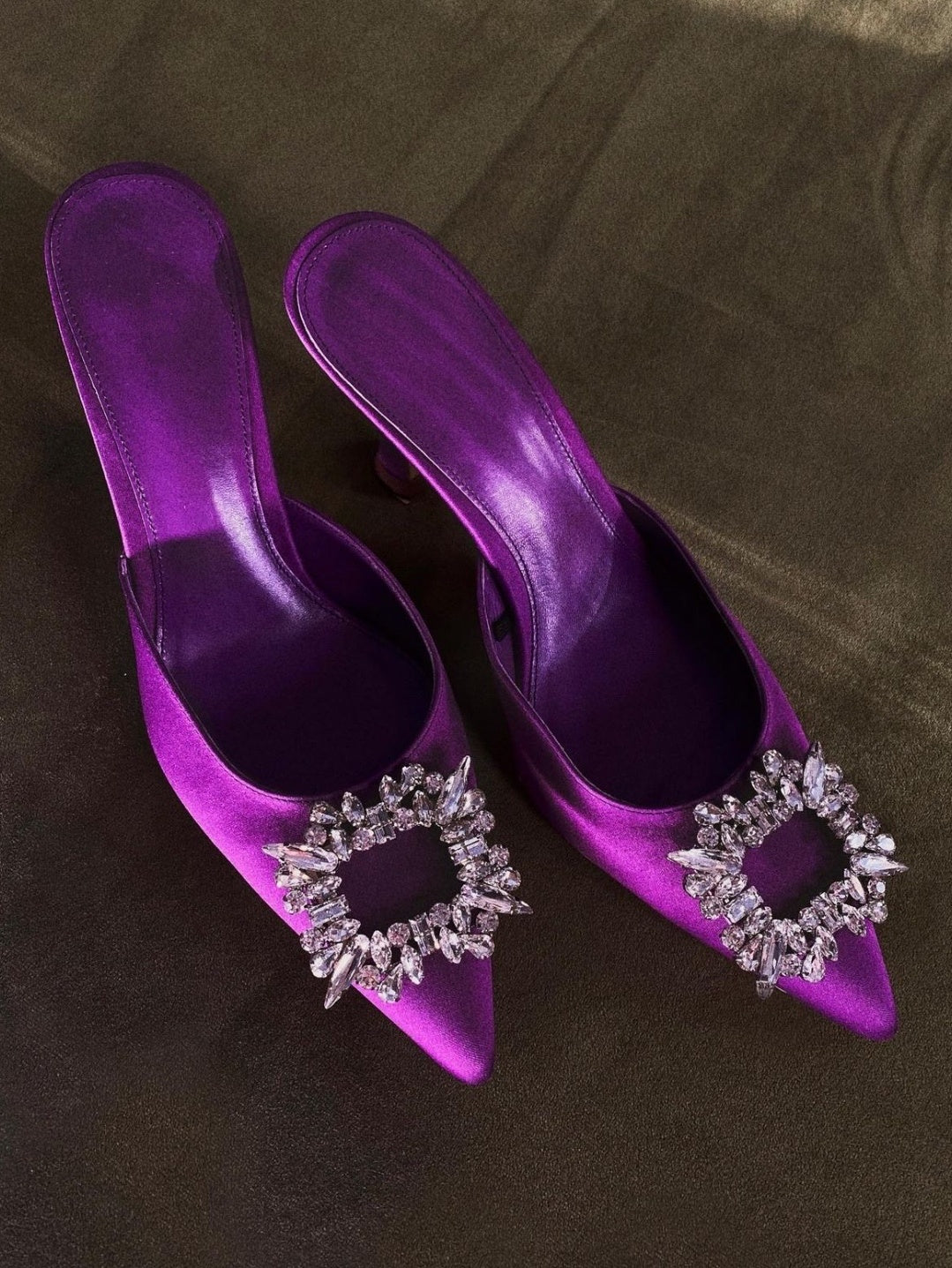 Purple high-heeled shoes with decorative embellishments on a brown surface