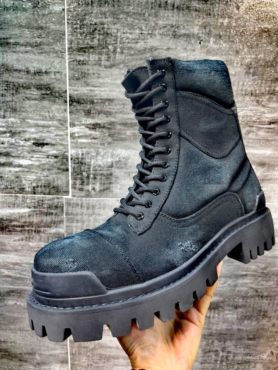 Black boot held by a hand against a textured gray background