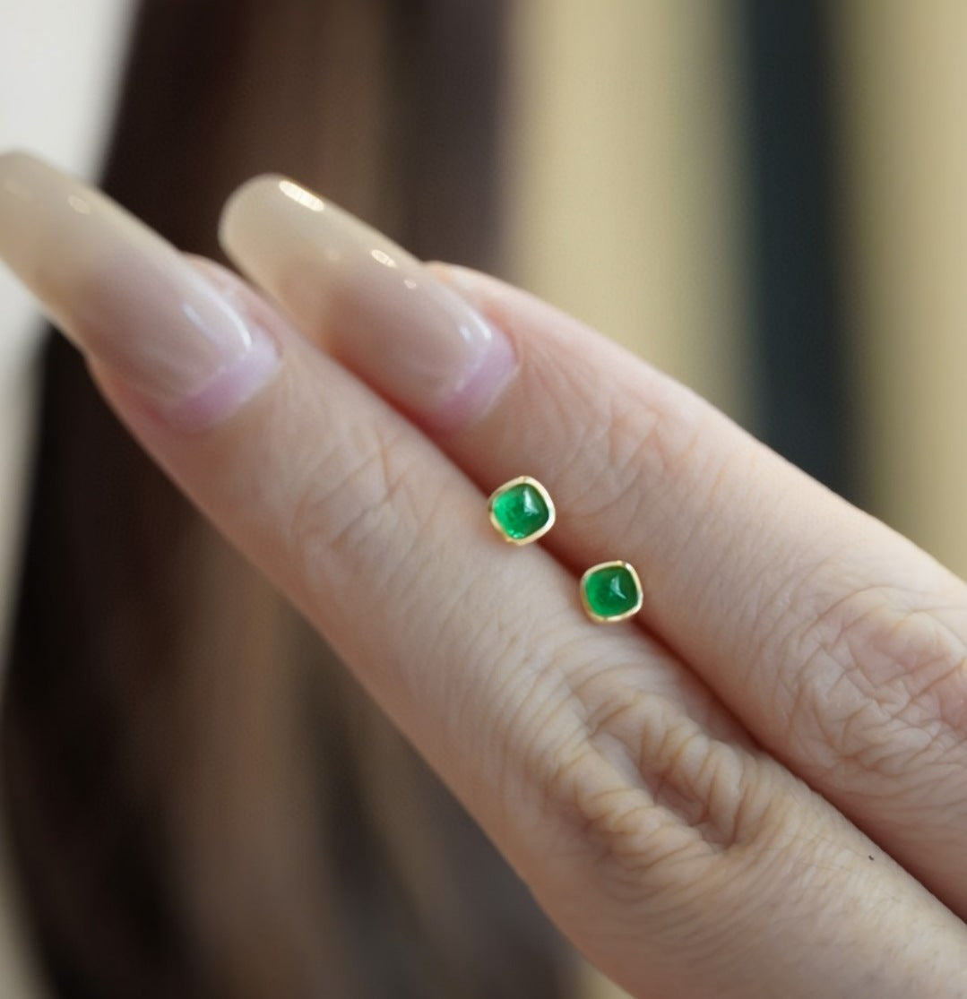 Green gemstone earrings on a finger with a blurred background