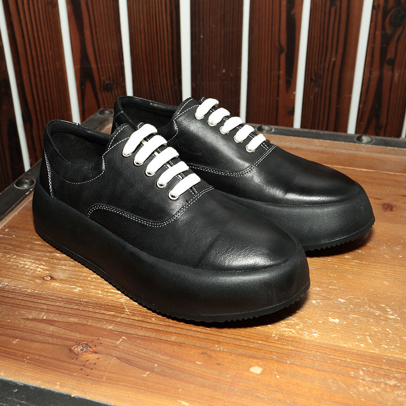 Black leather shoes with white laces on a wooden surface