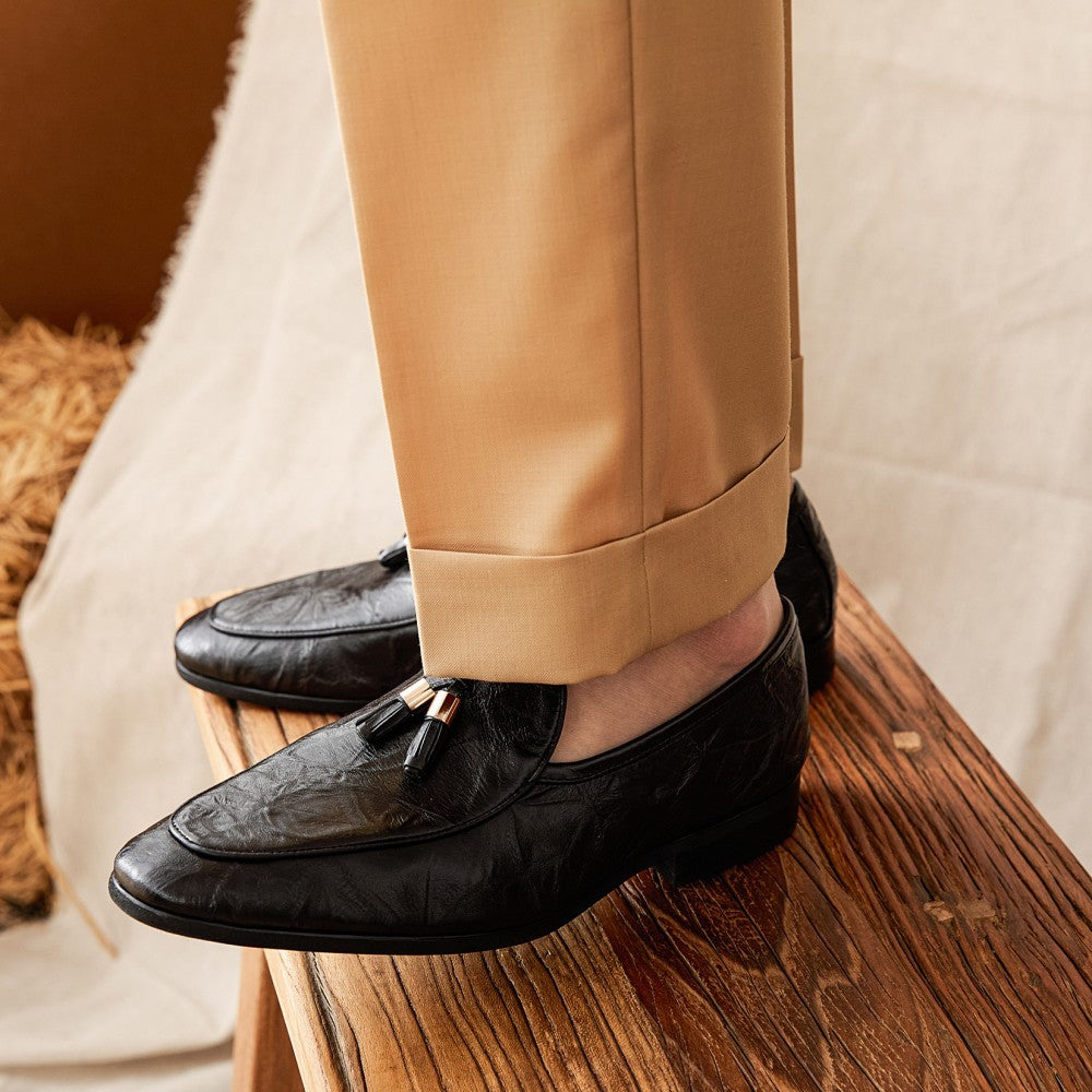 Black loafers worn with beige pants on a wooden surface