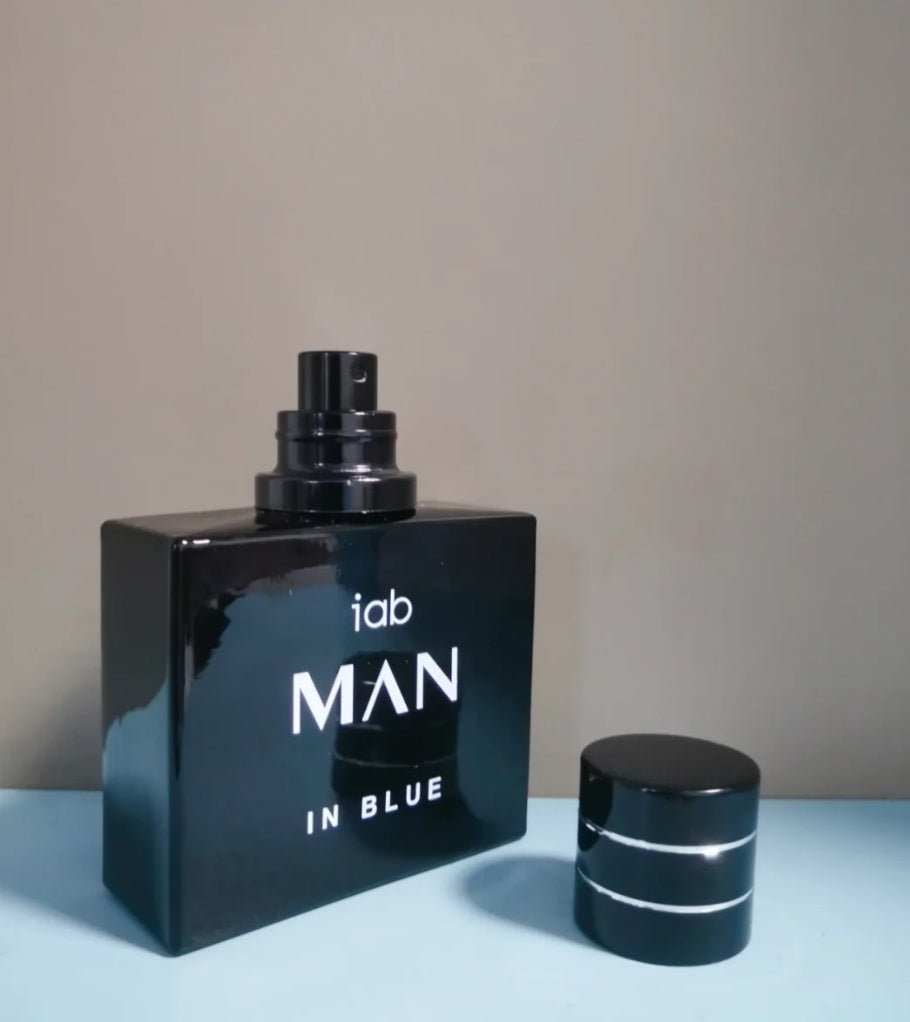 Black perfume bottle labeled 'Man in Blue' on a light blue surface with a beige background