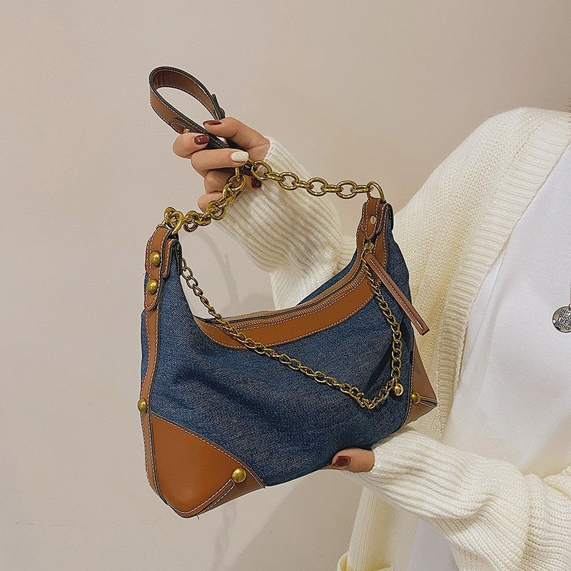 Denim handbag with gold chain handle held by a person wearing a white sweater.