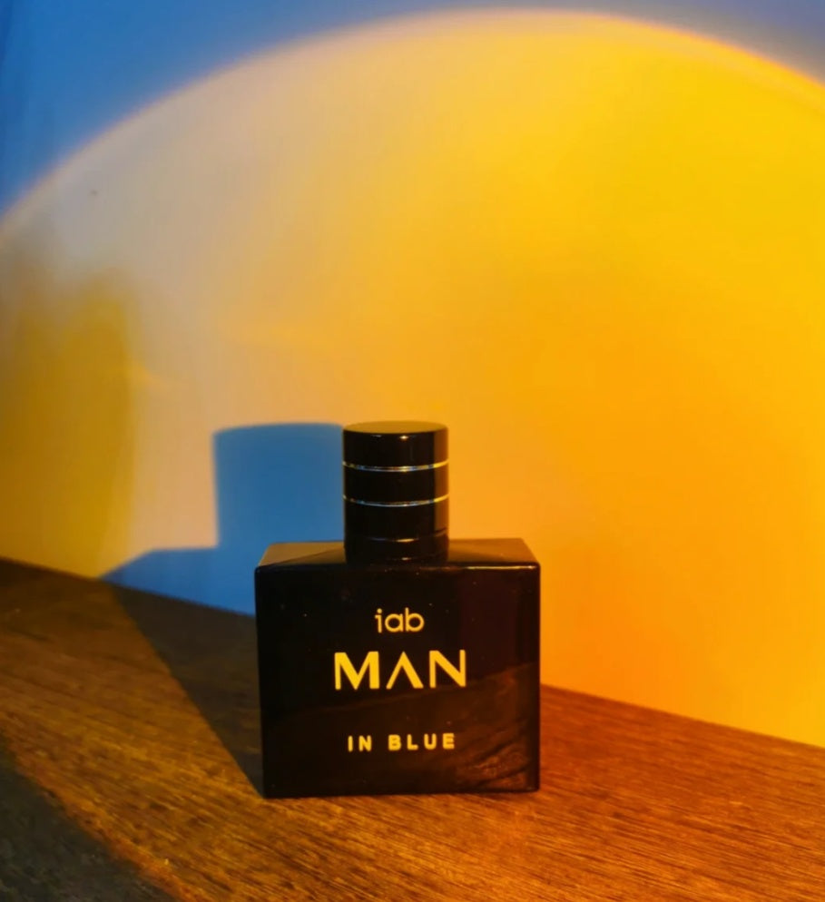 Black perfume bottle labeled 'iab MAN IN BLUE' on a wooden surface with a colorful background