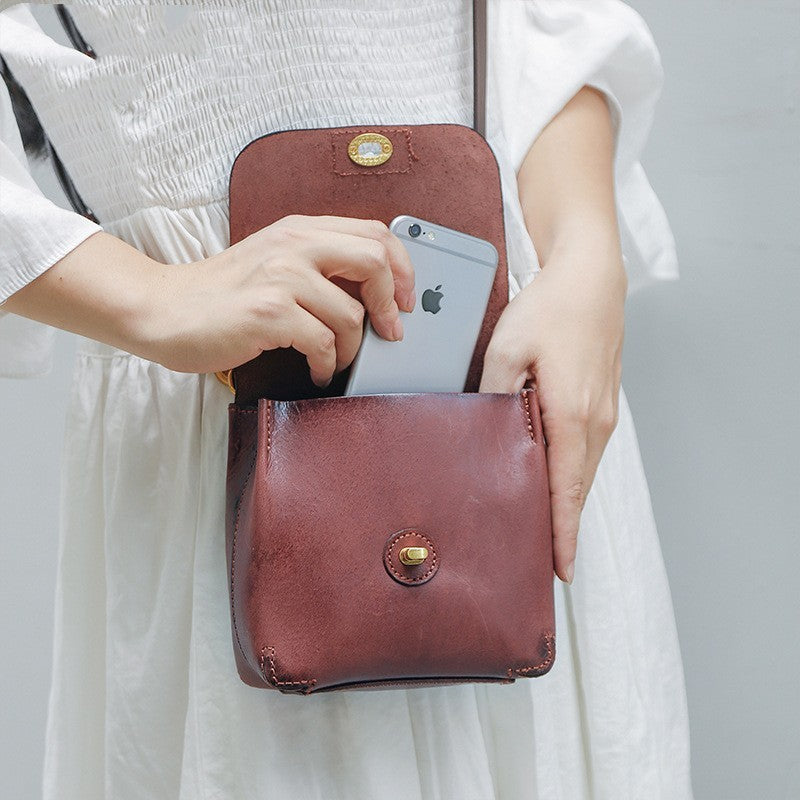 Person holding a brown leather crossbody bag with a phone inside, wearing a white dress.
