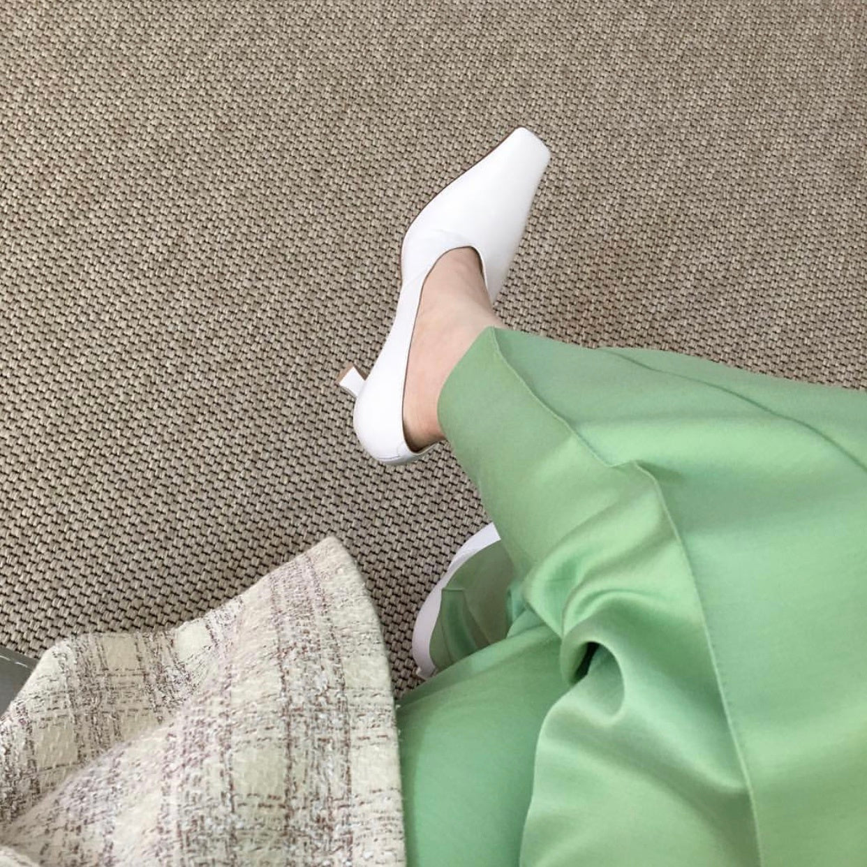 White pointed-toe shoes worn with green pants on a textured surface