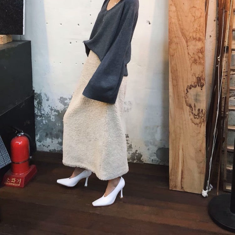 Person wearing a long beige coat and white shoes in a room with wooden walls and a fire extinguisher.
