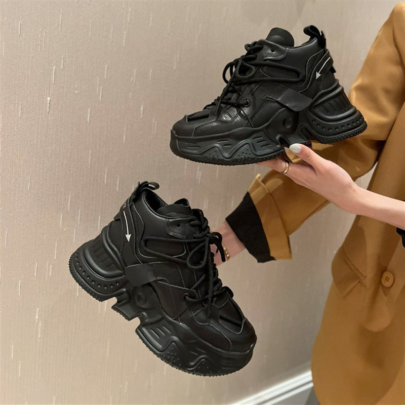 Person holding two black chunky sneakers against a neutral background
