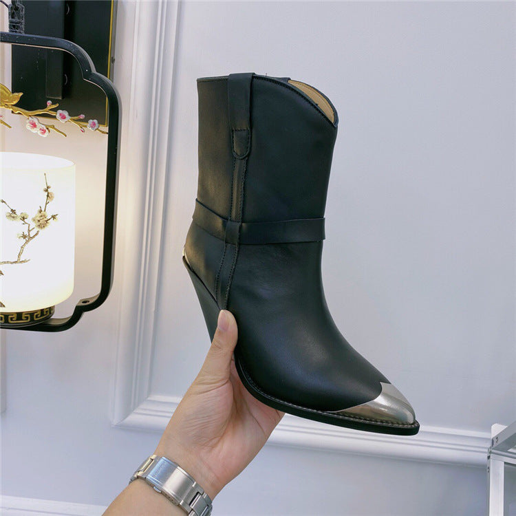 Black leather boot with metallic tip held by a hand against a light gray background