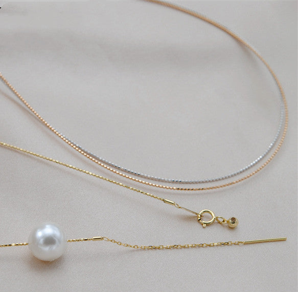 Gold and silver necklaces with a pearl on a light gray background