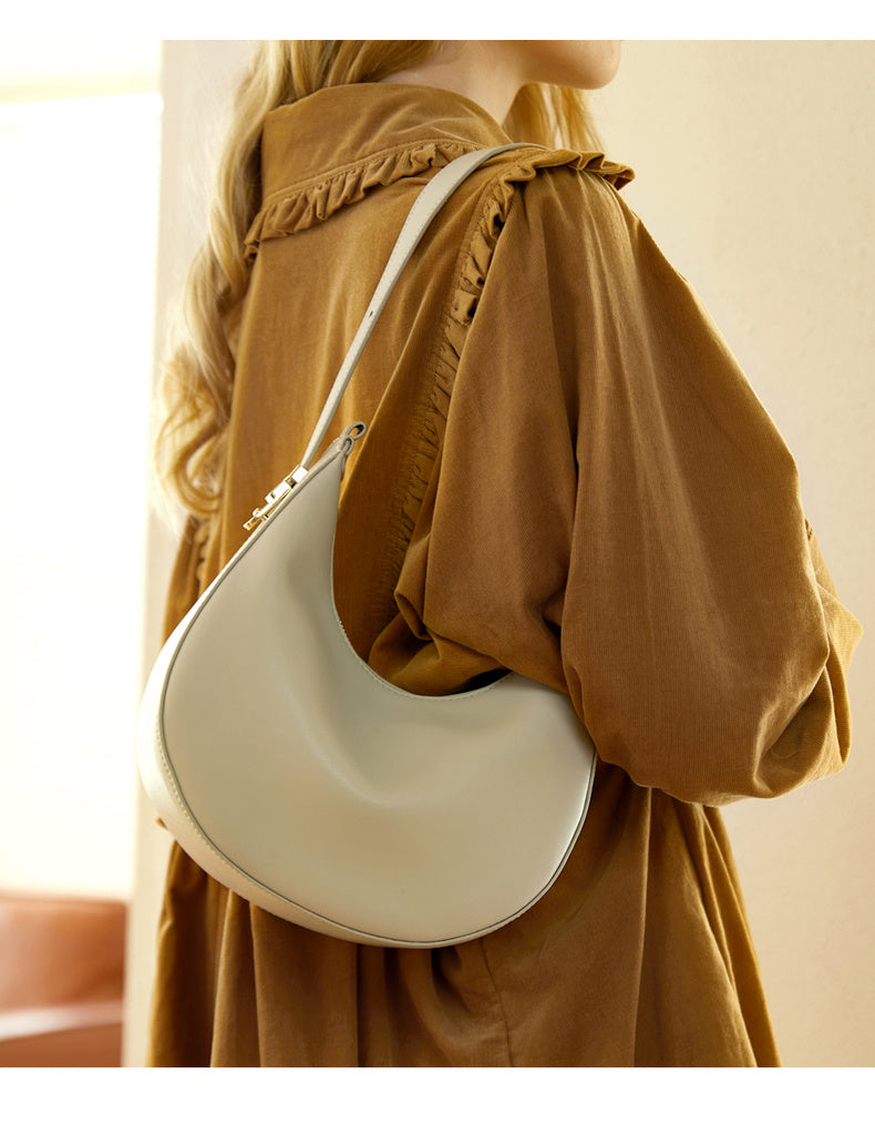 Person wearing a beige blouse with a white handbag on a neutral background