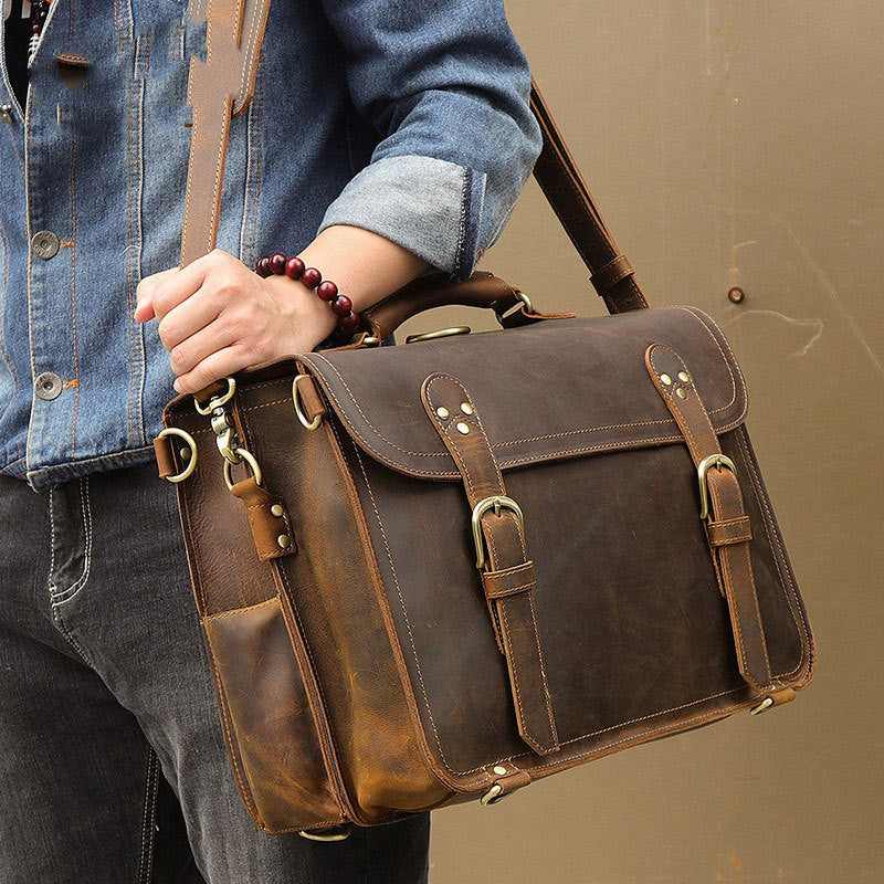 Person holding a brown leather satchel bag against a plain background